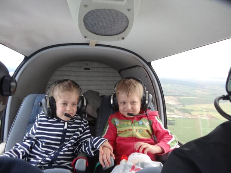 2 jeunes enfants assis à l'arrière d'un hélicoptère, portant chacun un casque sur la tête pour converser avec le pilote