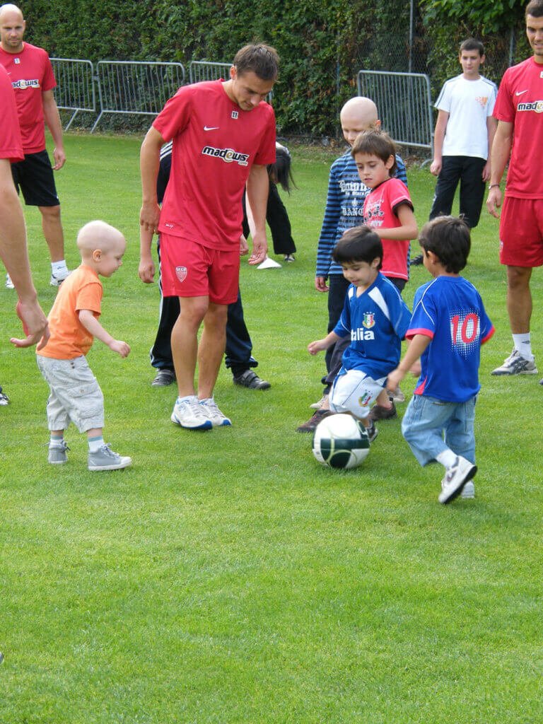 Jeunes enfants jouant au foot avec des joueurs du DFCO, portant leur maillot rouge