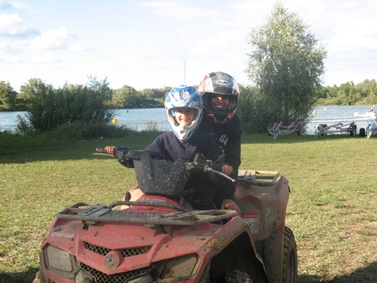 2 enfants portant un casque de moto sur la tête, assis sur un quad rouge